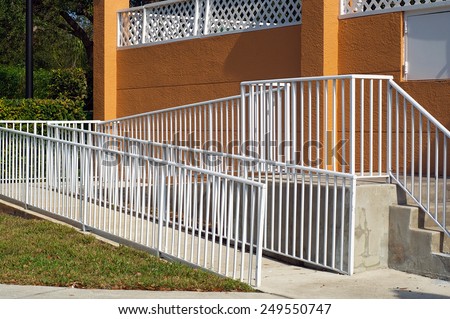 A white metal railing encloses a handicap ramp leading up to a building in Naples, Florida.