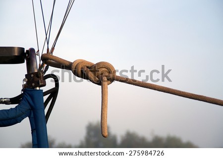 A strong rope is tied to the cables of a hot air balloon to hold it to the ground on a foggy morning. Balloon is not shown.