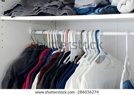 Looking inside a man\'s closet or armoire full of clothes hanging on hangers.