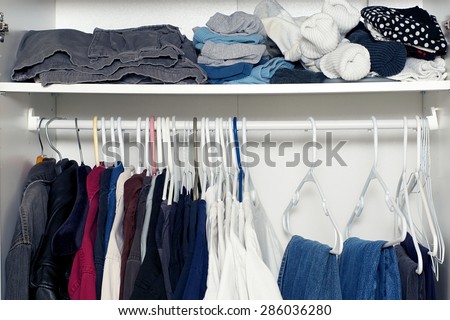 Looking inside a man\'s closet or armoire full of clothes hanging on hangers and laying on shelf.