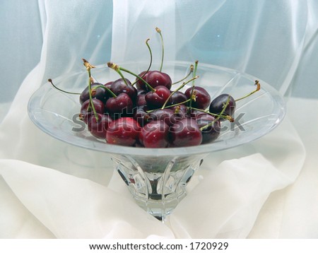 a glass bowl full of fresh cherries in front of a sheer curtain