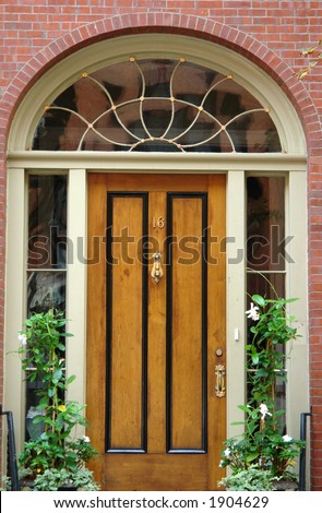 Natural woodgrain door with black trim, brass number and door knocker and handle, arched window above doorway  flower boxes on either side of door which is flanked by windows