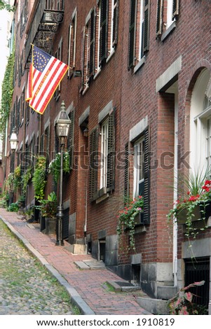 Walking up the cobblestone alley called Acorn Street lined with brick buildings, brick sidewalks old gas lanterns wooden shutters, flower boxes and an early american flag