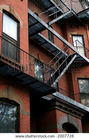 old fire escape zig zags down the side of an old brick apartment building in boston\'s beacon hill district