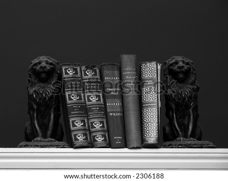A collection of scholarly books are held upon a shelf with two dust covered lion book ends. Black and white image