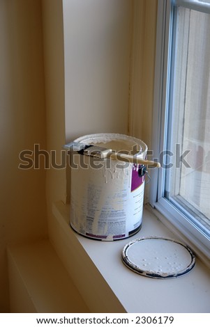 An open can of paint is sitting on a window sill with the paint covered brush sitting beside it. The paint in the room is the same color of the paint in the can. Room is lit by the natural sunlight.