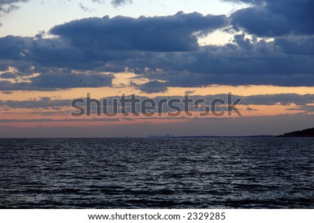 dramatic sunset over the atlantic ocean with deep thick clouds and ripples of the sea drawing the eye to the land mass in the background and the boston skyline
