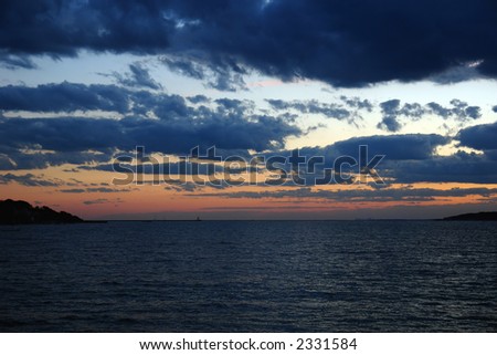 dramatic sunset over the atlantic ocean with deep thick clouds and ripples of the sea drawing the eye to the land mass on either side with the boston skyline in the distance