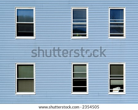 six windows on an apartment building in the sunshine, the building is covered in blue vinyl siding