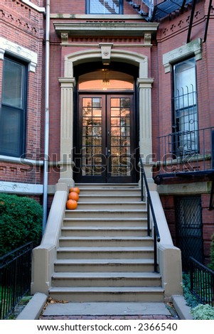 Brown french double doors sitting stately atop of cement stairs adorned with pumpkins