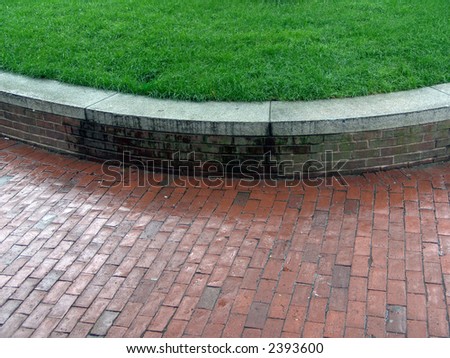 wet brick sidewalk with curving brick wall and raised lawn