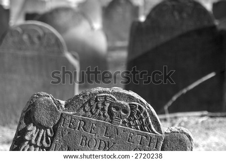 detail of top of tomb stone with others out of focus in the background, detail shows skull with wings