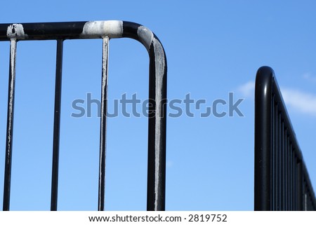 shiny black railings against a soft blue sky, with white paint at school playground