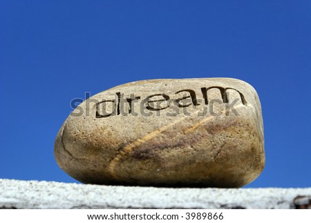 dreams put on the shelf, a rock with the word dream inscribed in it  sits on top of a brick wall against a deep blue sky