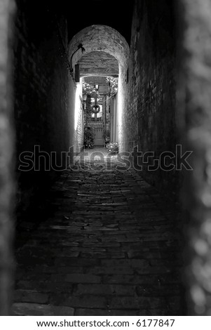 black and white image of doorway at the end of a spooky looking alley behind iron gate