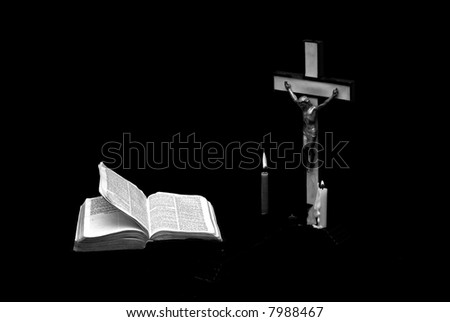stark somber black and white image of a prayer crucifix with two candles set out before a bible open to the book of matthew