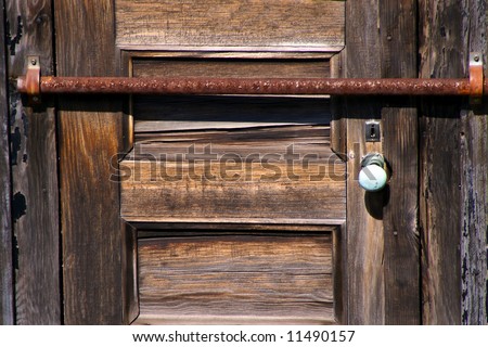 old door with is barred with rusty metal bar, white porcelain door knob and upside down keyhole
