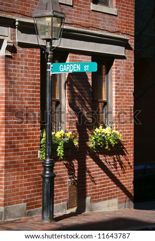 Garden street sign in bright sun light hangs from gas lamp post above two flower boxes with blooming flowers in beacon hill area of boston massachusetts