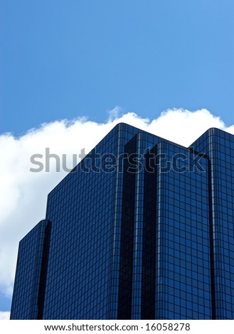 angular blue glass office building with rounded edges against clouds on a blue sky background