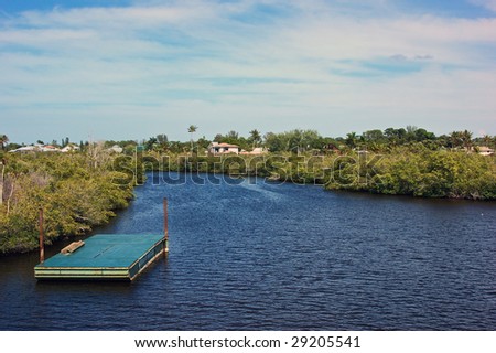 pier over water on a windy day with trees and houses in the background with  rippling water