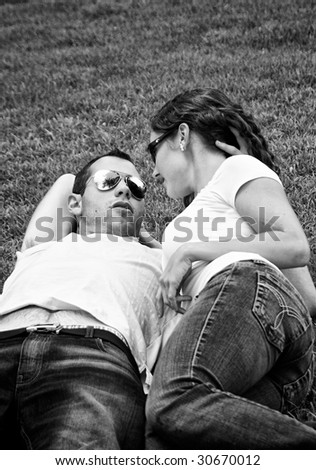 beautiful black and white of young punk lovers laying on the grass wearing sunglasses and talking