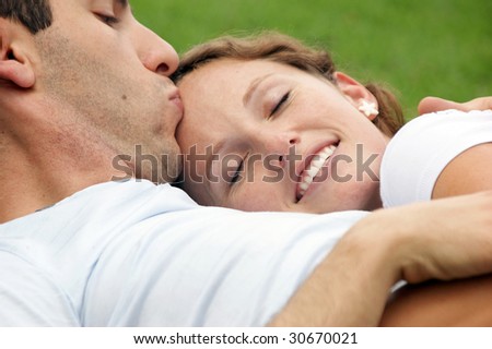 smiling woman with eyes closed resting her head on her husband\'s chest as he kisses her forehead