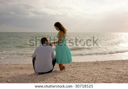 beautiful romantic image of couple on beach in the gulf of mexico looking at each other with the man kissing womans hand.  from behind with the ocean in front of them as the sun begins to set.
