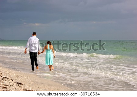 beautiful peaceful image of young couple walking along bonita beach in bonita springs florida on the gulf of mexico as the sun begins to set behind them