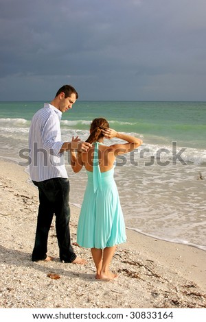 attractive young couple on beach in florida having a discussion with waves crashing in front of them. she is fixing her hair, he appears to be listening