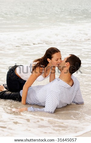 beautiful young couple  at the beach, about to kiss as the tide comes up and covers them with water, getting washed away.