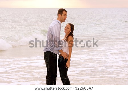 fully clothed and soaking wet from the ocean this young couple are laughing and having fun while holding each other