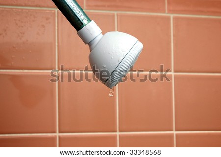 a white plastic showerhead attached to a rusty metal pipe is leaking, bathroom wall tiles are in the background
