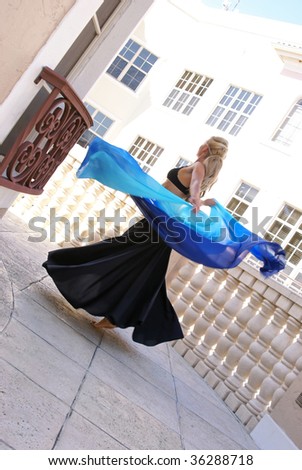 beautiful blonde belly dancer spinning around with veil on balcony outside buildings