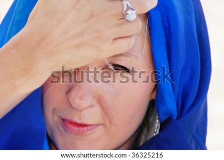 beautiful woman with brown eyes with hand over forehead looking concerned or worried with her head covered in blue silk