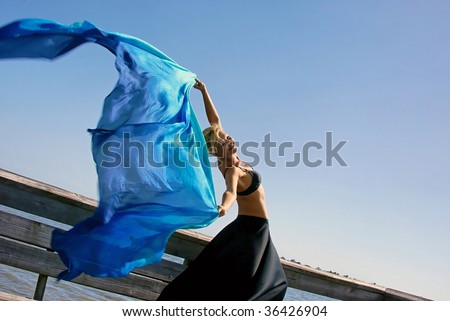 attractive fit blonde woman is happily leaning back holding her arms up and letting a beautiful silk cloth flow through the air behind her with room for copy or text