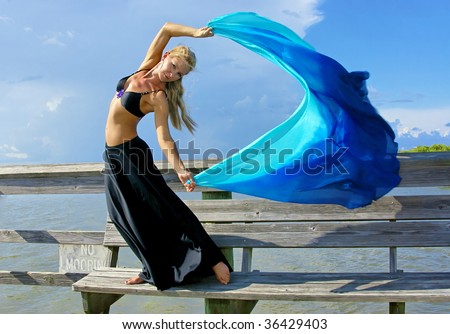 a beautiful blonde fit and trim belly dancer strikes a dramatic pose as the wind blows he hair, skirt, and veil