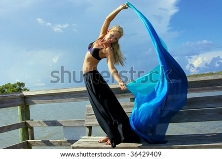 a beautiful blonde dancer making eye contact with her arms raised and her torso twisted towards the viewer, with room for copy or text