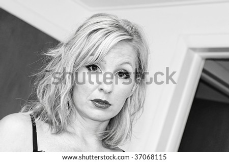 attractive blonde woman with messy hair and big eyes is looking directly at viewer with doorways in the background making it feel like a candid image, black and white