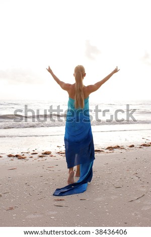 a long haired blonde woman is turned away from the viewer with her arms raised up to the sky as if worshiping the sun