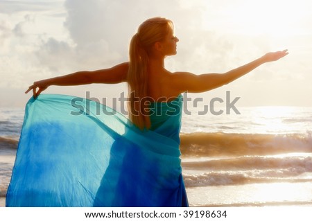beautiful woman from behind as she has her hand outstretched as if holding the sun and looking at it in a goddess like pose.