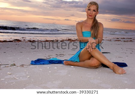 woman sitting cross legged on beach looking directly at the viewer, her legs are crossed and her hands are resting on her knees. with copy space.