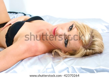 beautiful woman laying down on satin sheets looking up at viewer wearing bra and panties.