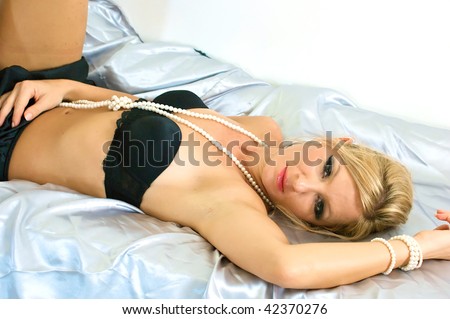 beautiful woman laying down on satin sheets looking at viewer wearing underwear and resting her hand on her stomach.