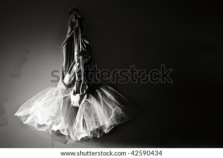 sepia toned image of tutu and ballet slippers hanging on wall lit from sunlight on the left with plenty of space for copy or text.