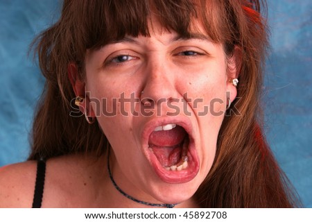 a beautiful woman with long brown hair is making a funny face or yelling at the viewer with mouth open wide, shot with red and blue strobes to enhance colors.