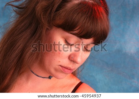 a beautiful young woman has her eyes and head lowered as she looks to the side, shot with red and blue strobes to enhance colors.