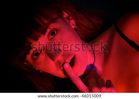 beautiful woman with finger to lips lit in red and looking like she was caught being naughty, shot with intense red strobe for effect.