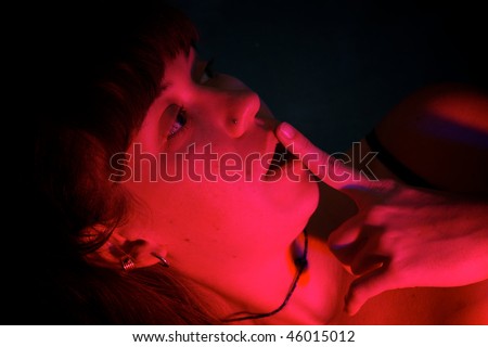 A beautiful woman is looking to the side with finger on lips looking as if she sees something bad,  shot with intense red strobe for effect.