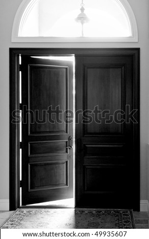Black and white image of large dark wooden entry doors with arched window above