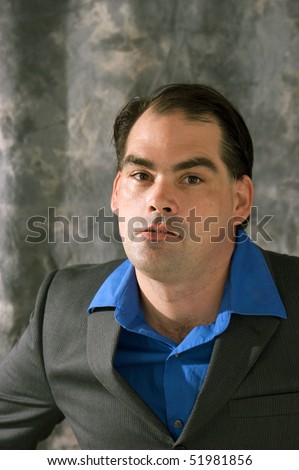 side lit man in suit and open collar looking irritated at viewer